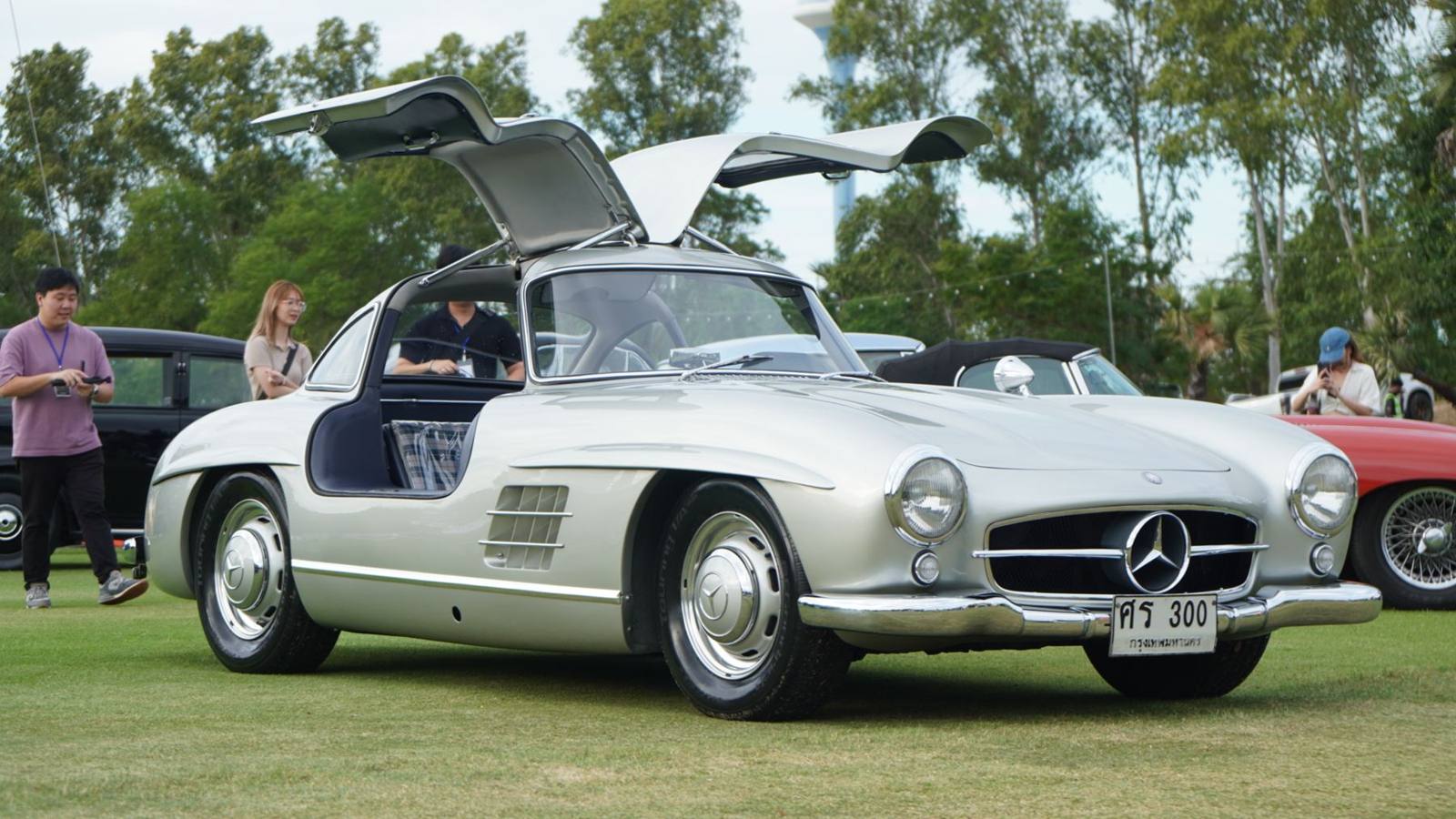 Silver Mercedes 300 SL Gullwing with its doors open on the lawn at a concours